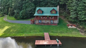 A log cabin with a green roof, a stone chimney, and a deck with outdoor seating. - Waterfront Home in Picturesque Community (Jefferson)