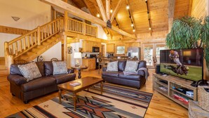 A spacious living room with two leather sofas, a coffee table, and a TV. A wooden staircase leads to an upper level. - Waterfront Home in Picturesque Community (Jefferson)