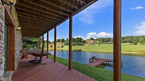 A wooden deck with a hammock, a stone building, and a view of a lake and hills. - Waterfront Home in Picturesque Community (Jefferson)