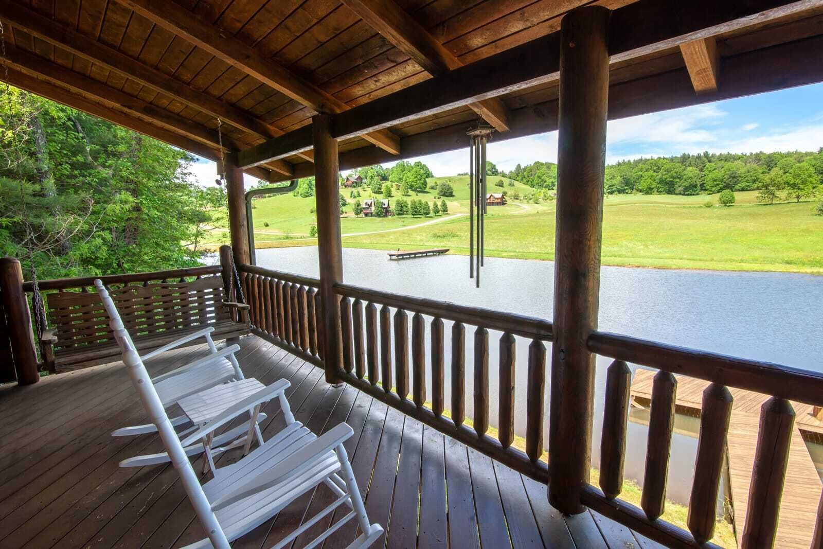 Una terraza de madera con sillas blancas que da a un lago y un campo de golf.