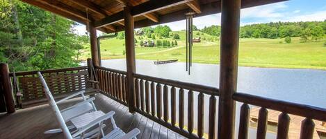 Una terraza de madera con sillas blancas que da a un lago y un campo de golf.