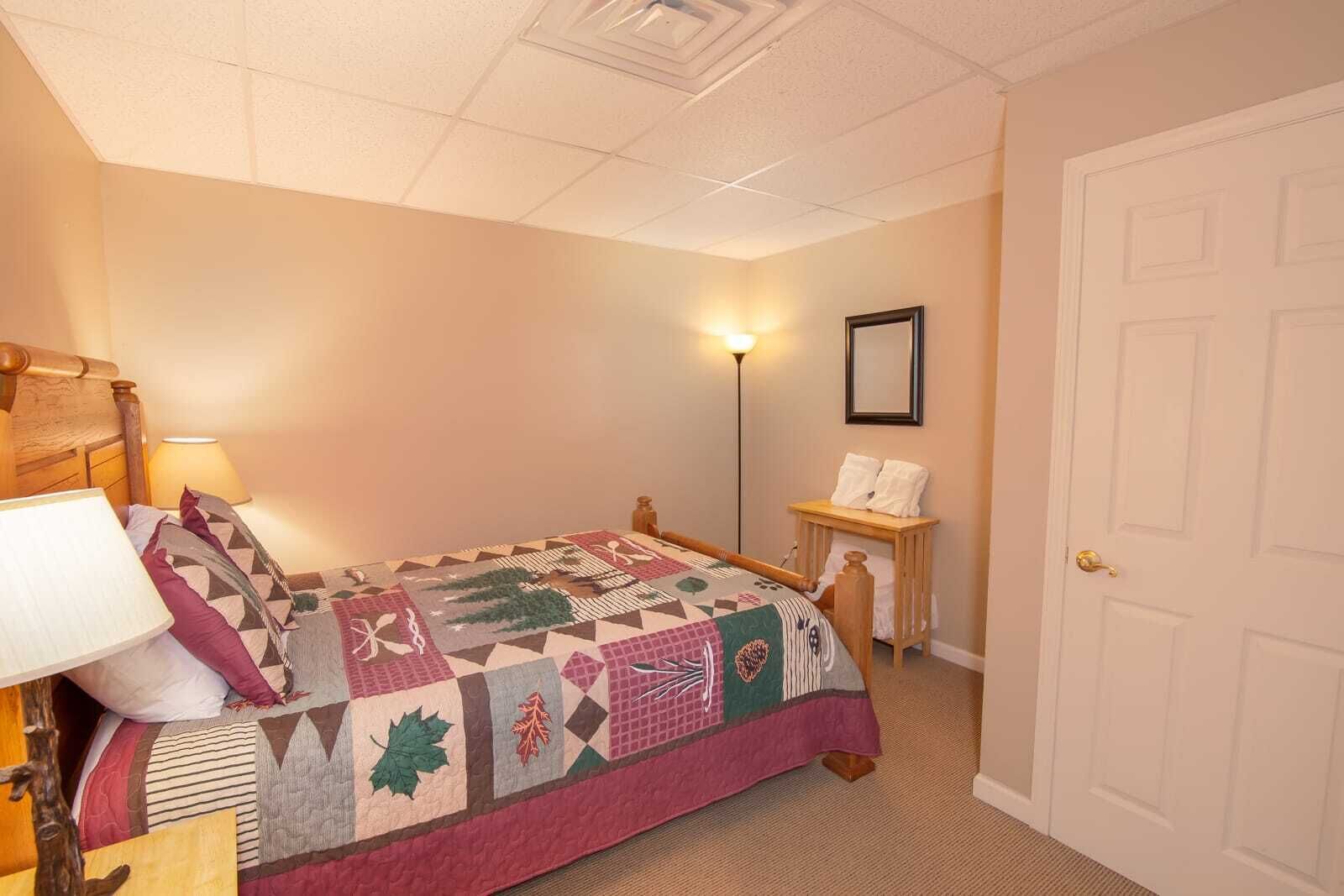 A bedroom with a bed, a nightstand, a lamp, a framed picture on the wall, and a door.