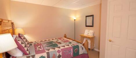 A bedroom with a bed, a nightstand, a lamp, a framed picture on the wall, and a door.