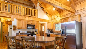 A spacious kitchen with wooden cabinets, a large island with chairs, a stainless steel refrigerator, and a wooden ceiling. - Waterfront Home in Picturesque Community (Jefferson)