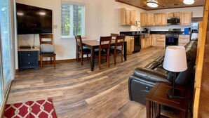 A modern kitchen with wooden cabinets, a dining area with a table and chairs, a leather sofa, and a TV on a stand. - Incredible View, Privacy & Private hot tub! (Homer)
