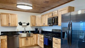 A modern kitchen with wooden cabinets, stainless steel appliances, a built-in oven, and a refrigerator. - Incredible View, Privacy & Private hot tub! (Homer)