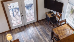 A room with a wooden floor, a desk with a chair, a TV mounted on the wall, and a door with glass panels. - Incredible View, Privacy & Private hot tub! (Homer)