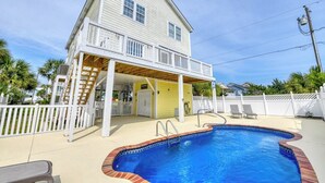 Una casa de dos pisos con piscina, un porche cubierto y un patio cercado.