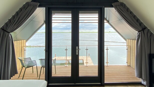 Une pièce dotée d’une grande porte-fenêtre coulissante donnant sur une terrasse extérieure avec vue sur un plan d’eau.
