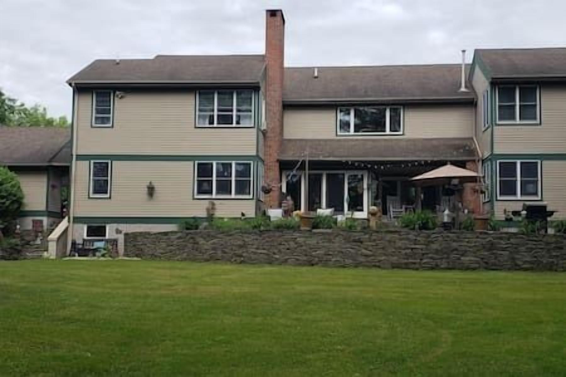 Una casa de dos pisos con base de piedra, una chimenea y un patio cubierto con mobiliario exterior.