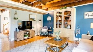 A cozy living room with a wooden ceiling, a television, a bookshelf, and a coffee table.