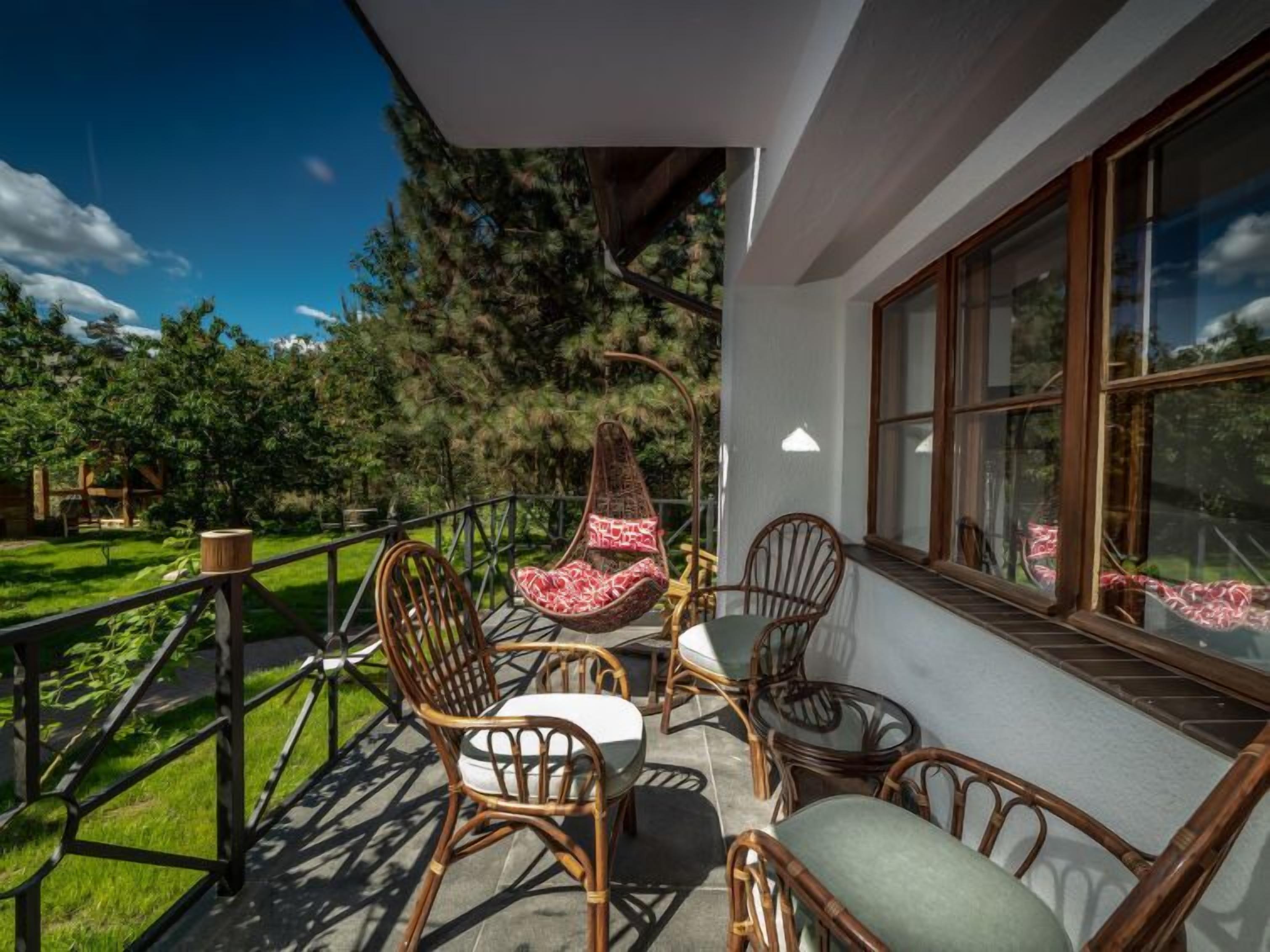 Ein Balkon mit Korbstühlen und einem Tisch, mit Blick auf einen üppigen Garten und ein bewaldetes Gebiet.