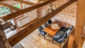 A loft-style room with exposed wooden beams, a herringbone-patterned floor, a brick wall, and a hanging light fixture.
