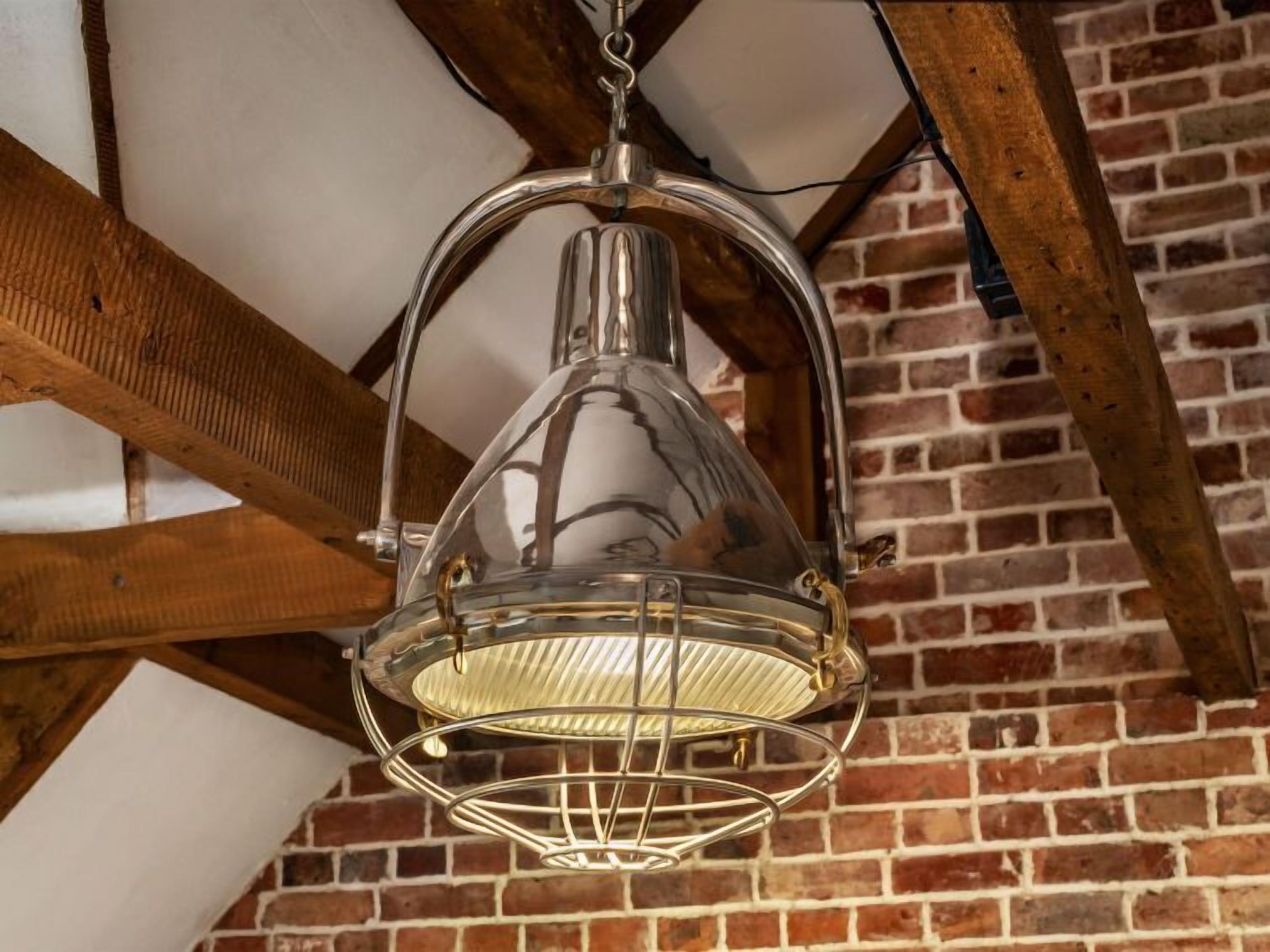 Une lanterne métallique suspendue, dotée d’un intérieur à nervures, et fixée à une structure en poutres de bois.