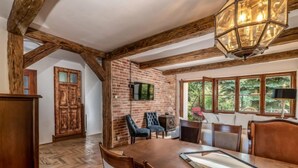 A dining area with a wooden table and chairs, a brick wall, and a large window with a view of greenery.