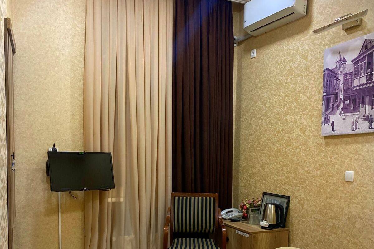 A hotel room with a bed, a chair, a desk with a telephone, a picture frame, and an air conditioning unit.