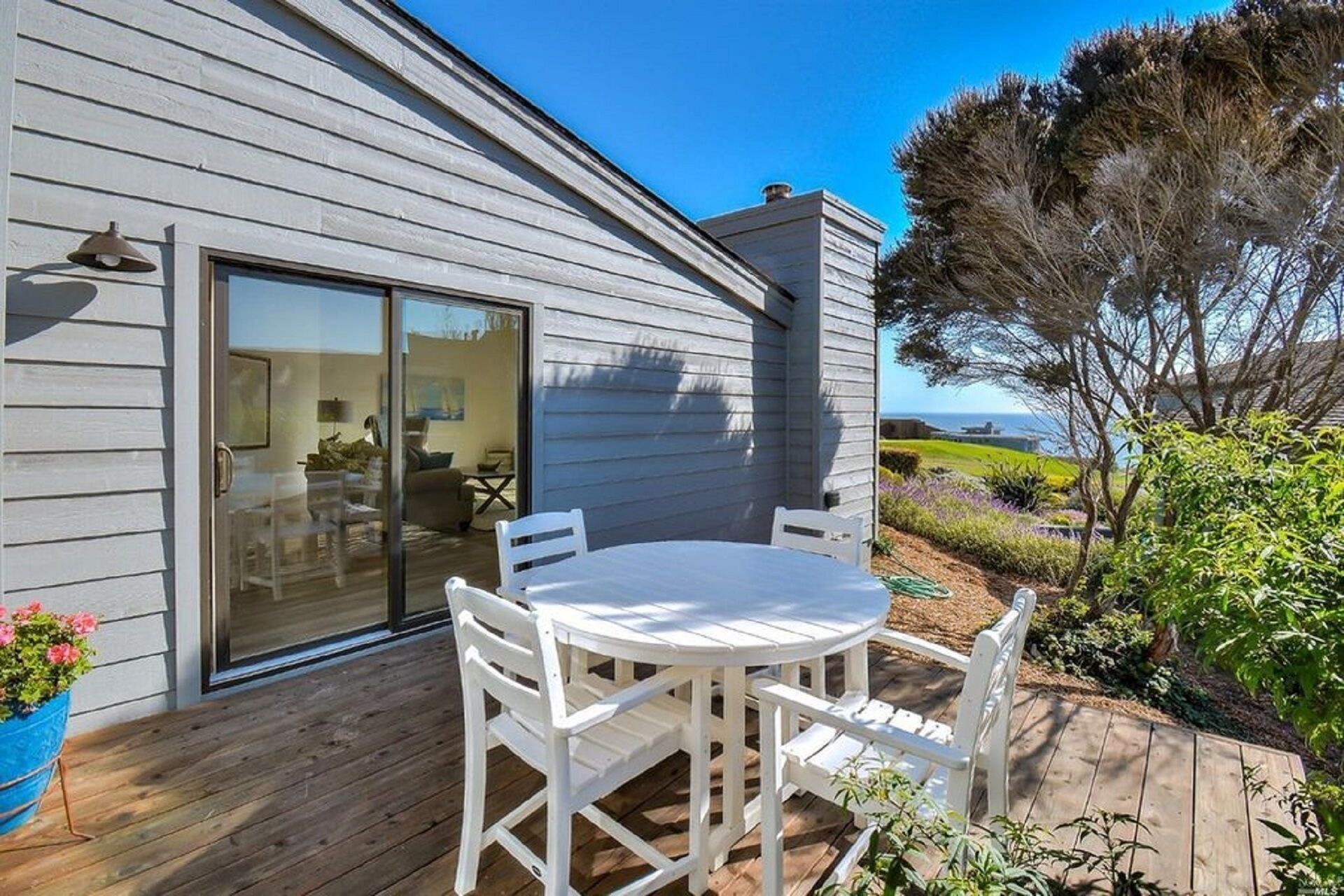 A deck with a round table and chairs, a sliding glass door leading to an interior space, and a view of the ocean.