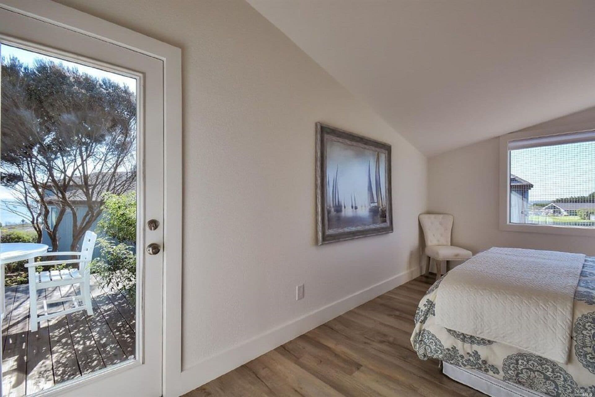 A bedroom with a bed, a chair, a painting, and a view of the outdoors.