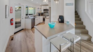 A modern kitchen with white cabinetry, a central island with bar stools, a fire extinguisher, and a sign on the wall. - Ocean view easy access to Doran Beach, Golf  course and  Bluewater Bistro. (Bodega Bay)