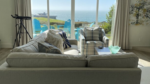 A spacious living room with a large sofa, a telescope, and a view of the ocean. - Ocean view easy access to Doran Beach, Golf  course and  Bluewater Bistro. (Bodega Bay)