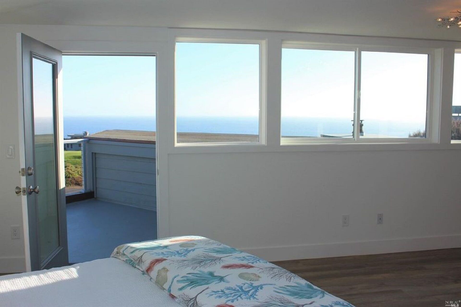 A bedroom with a large window, a bed, and a view of the ocean.