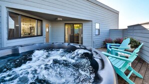 A hot tub with a wooden deck, a covered patio area, and a house with large windows and a door. - Ocean view easy access to Doran Beach, Golf  course and  Bluewater Bistro. (Bodega Bay)