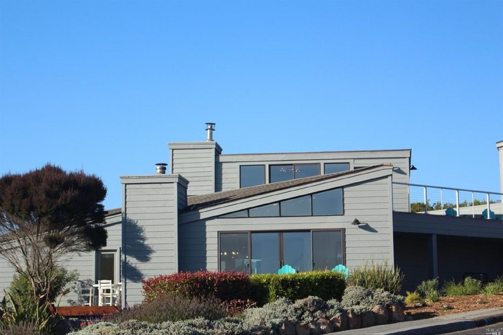 A modern two-story house with a sloped roof, large windows, and a small balcony.