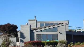A modern two-story house with a sloped roof, large windows, and a small balcony.
