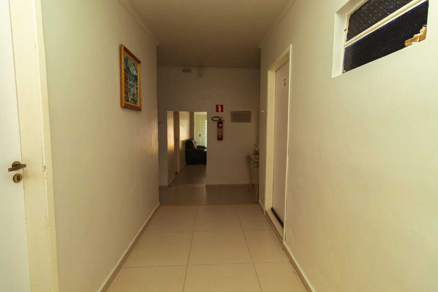 Un passadís estret amb parets blanques, un sòl de rajoles, una porta a l'esquerra i una finestra a la dreta.