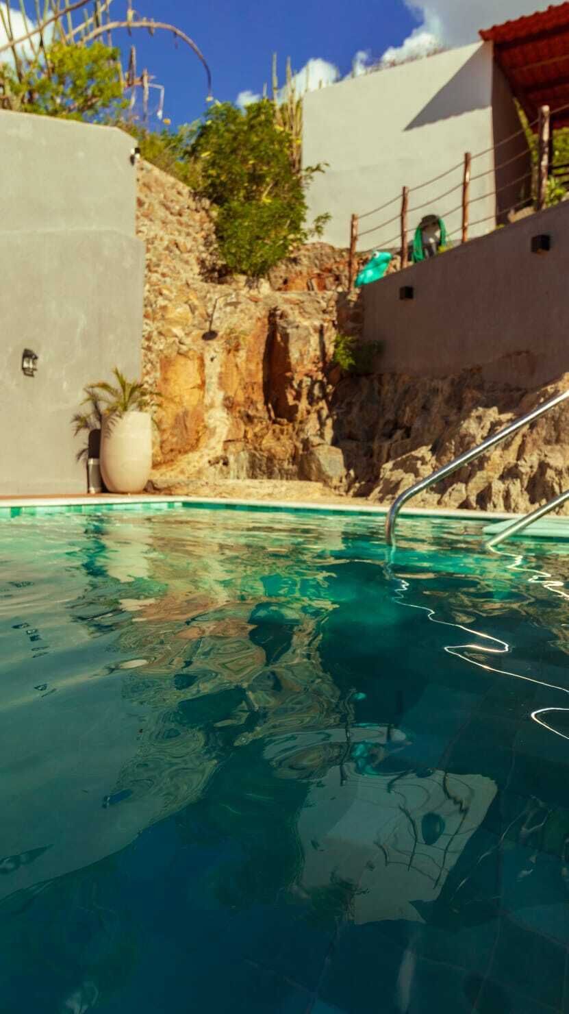 A swimming pool with clear water, a stone wall, and a metal ladder.