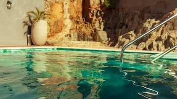 A swimming pool with clear water, a stone wall, and a metal ladder.