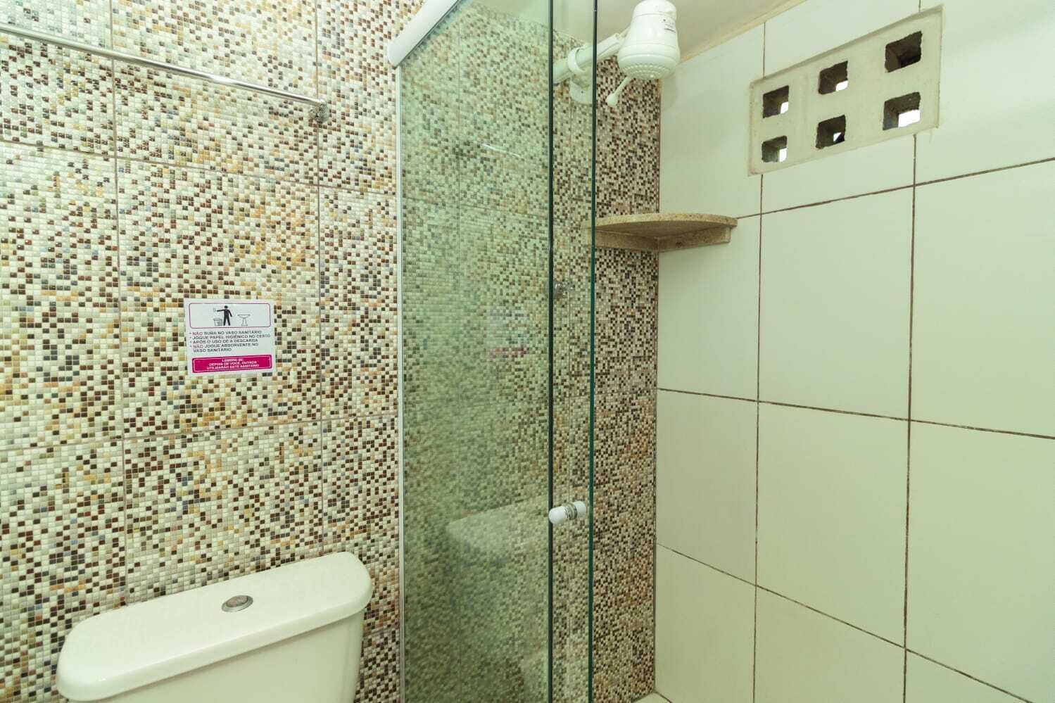 Un baño con pared de mosaicos, cabina de ducha de vidrio y un inodoro.