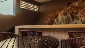 A modern interior with a round wooden table and wicker chairs, a stone wall, and a ceiling light fixture.