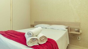 A hotel room with a bed, a red blanket, and two rolled towels.