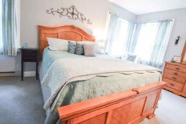 Un dormitorio con cama de madera, mesita de noche, cómoda y un adorno en la pared.