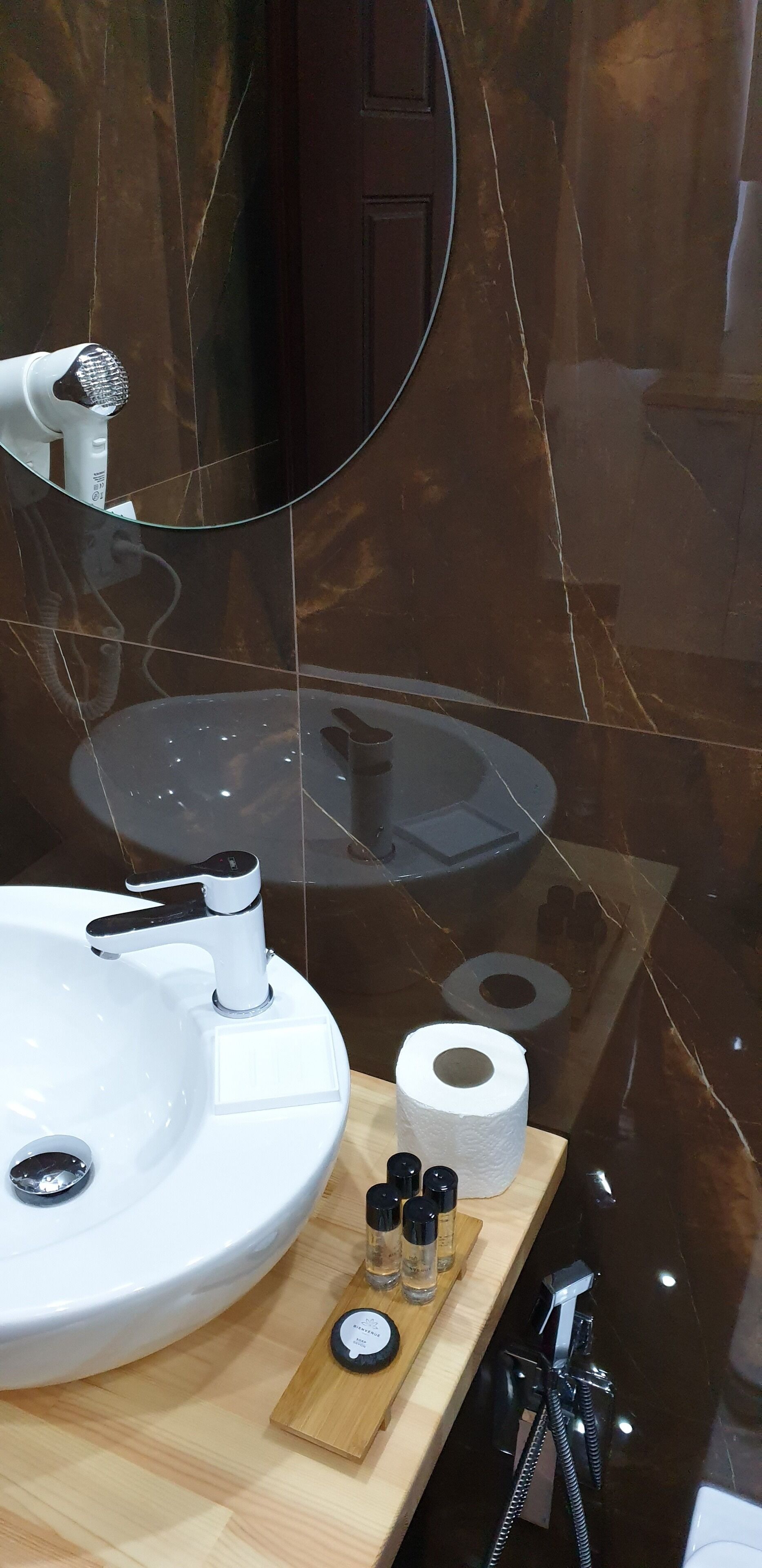 A bathroom with a white sink, a mirror, and a wooden shelf with toiletries.
