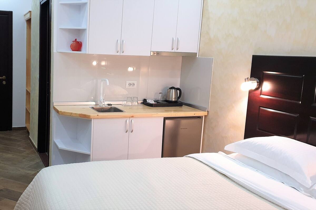Une chambre d’hôtel de taille réduite, comprenant un lit, une petite kitchenette, une table en bois et une chaise.