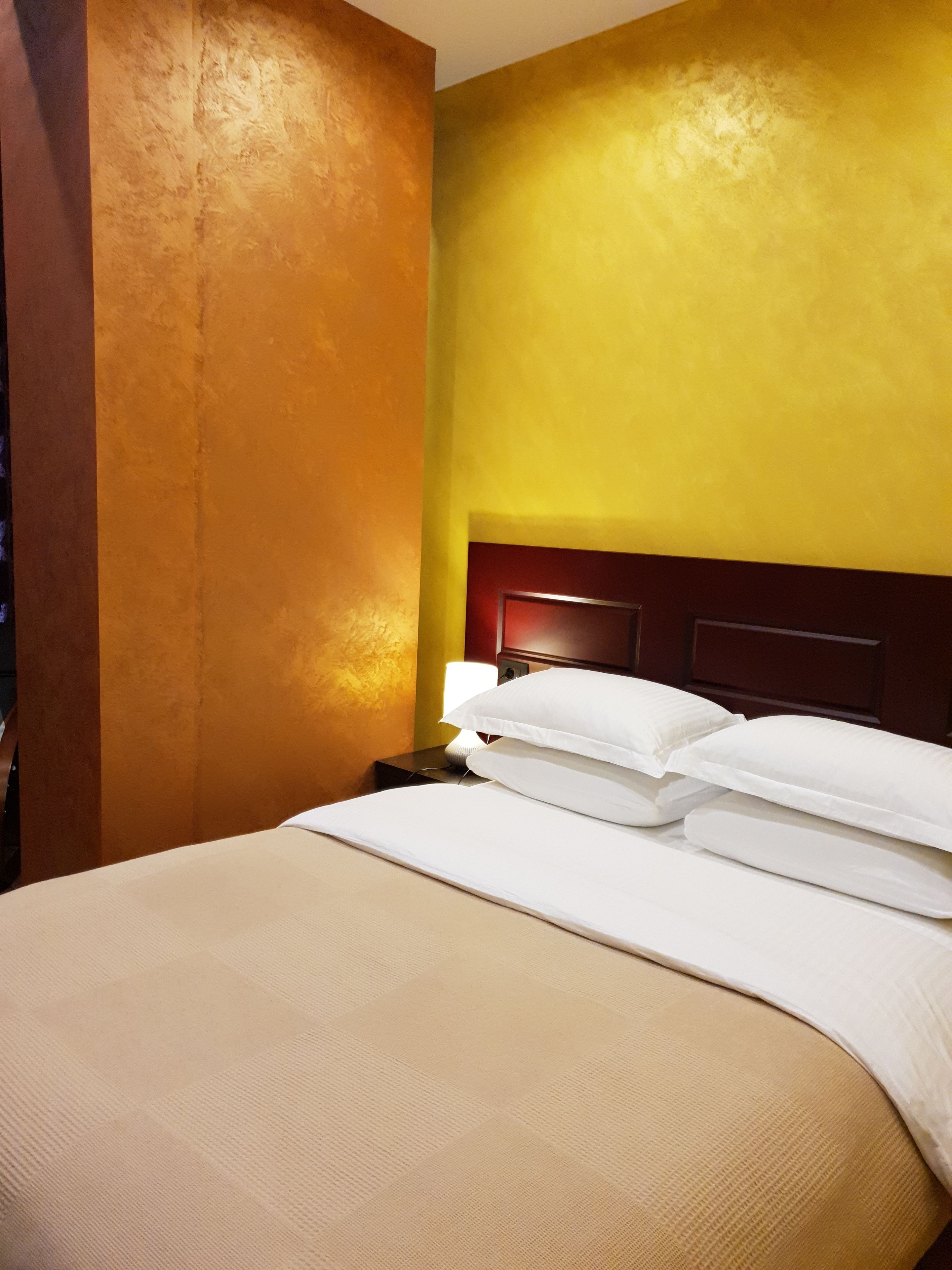 A hotel room with a bed, a nightstand, and a lamp.