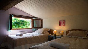 A room with two beds, a window with curtains, a lamp on a bedside table, and a painting on the wall. - Nature's Pace Holidays (Montmaur)