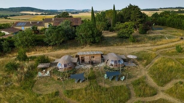 A rural setting with a small house and two dome-shaped structures, possibly yurts, with outdoor seating and a path leading to them. - Nature's Pace Holidays (Montmaur)