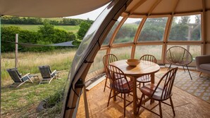 A cozy interior with a round wooden table and chairs, large windows offering a view of the outdoors, and a hammock outside. - Nature's Pace Holidays (Montmaur)