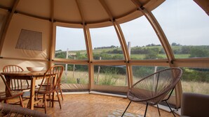 A tent with a wooden table and chairs, a woven chair, and a view of the countryside. - Nature's Pace Holidays (Montmaur)