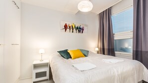 Une chambre moderne avec un grand lit, une table de chevet avec une lampe, une œuvre d’art représentant des oiseaux accrochée au mur et une fenêtre avec des rideaux.
