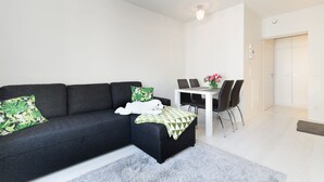 Un salon moderne avec un canapé foncé, une table à manger blanche et un tapis gris.