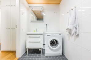 A compact, modern bathroom with a white sink, a washing machine, and a mirror above the sink. - Go Happy Home Apartment Mikonkatu 11 55 (Helsinki)