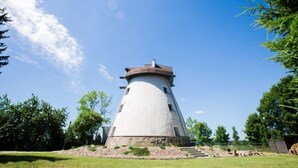 Ein zylindrischer Leuchtturm mit einer kegelförmigen Kuppel, umgeben von einer grünen Wiese und Bäumen.