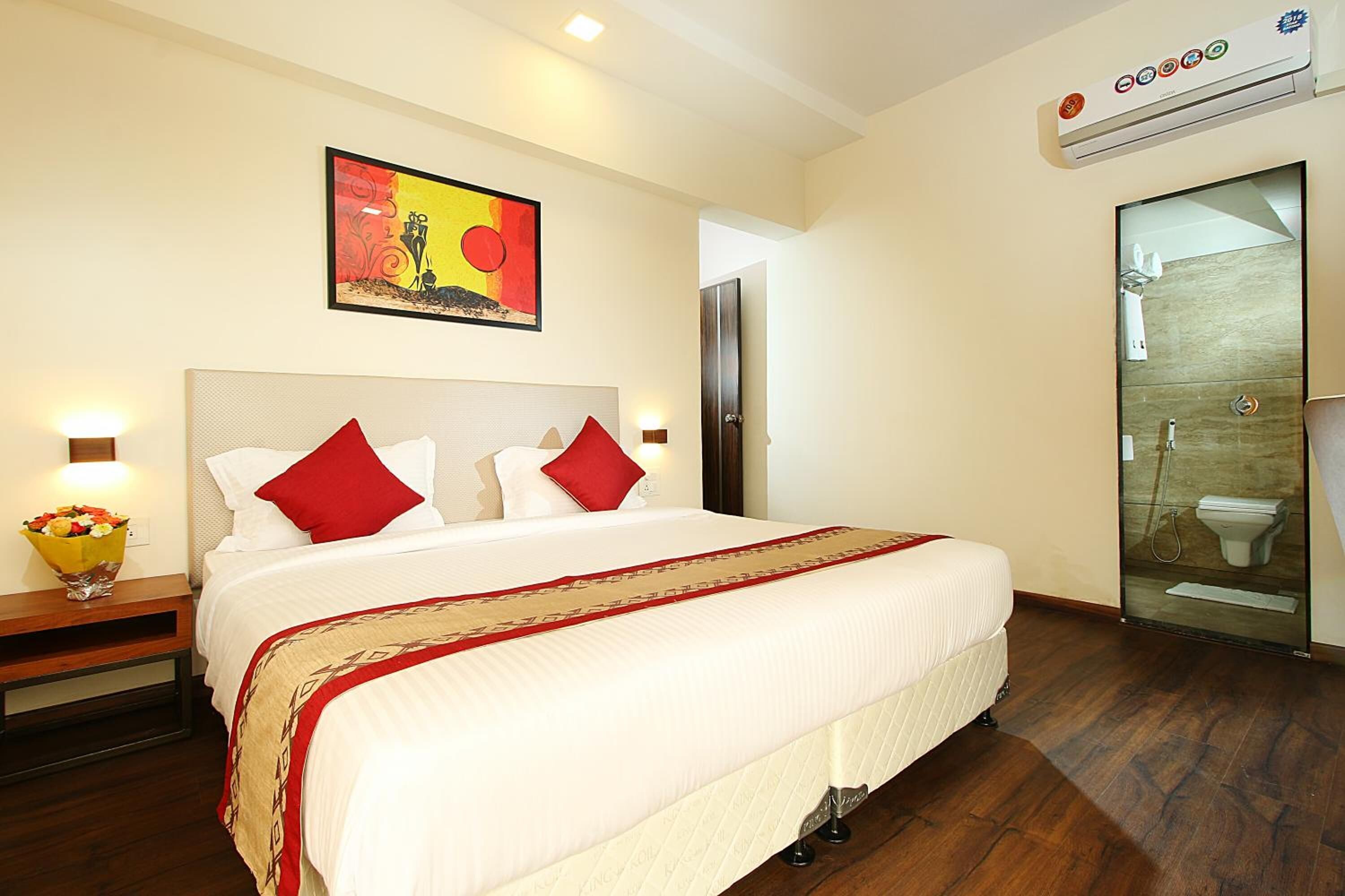 Habitación de hotel con una cama grande, un cuadro en la pared, un equipo de aire acondicionado y un baño con cabina de ducha de vidrio.