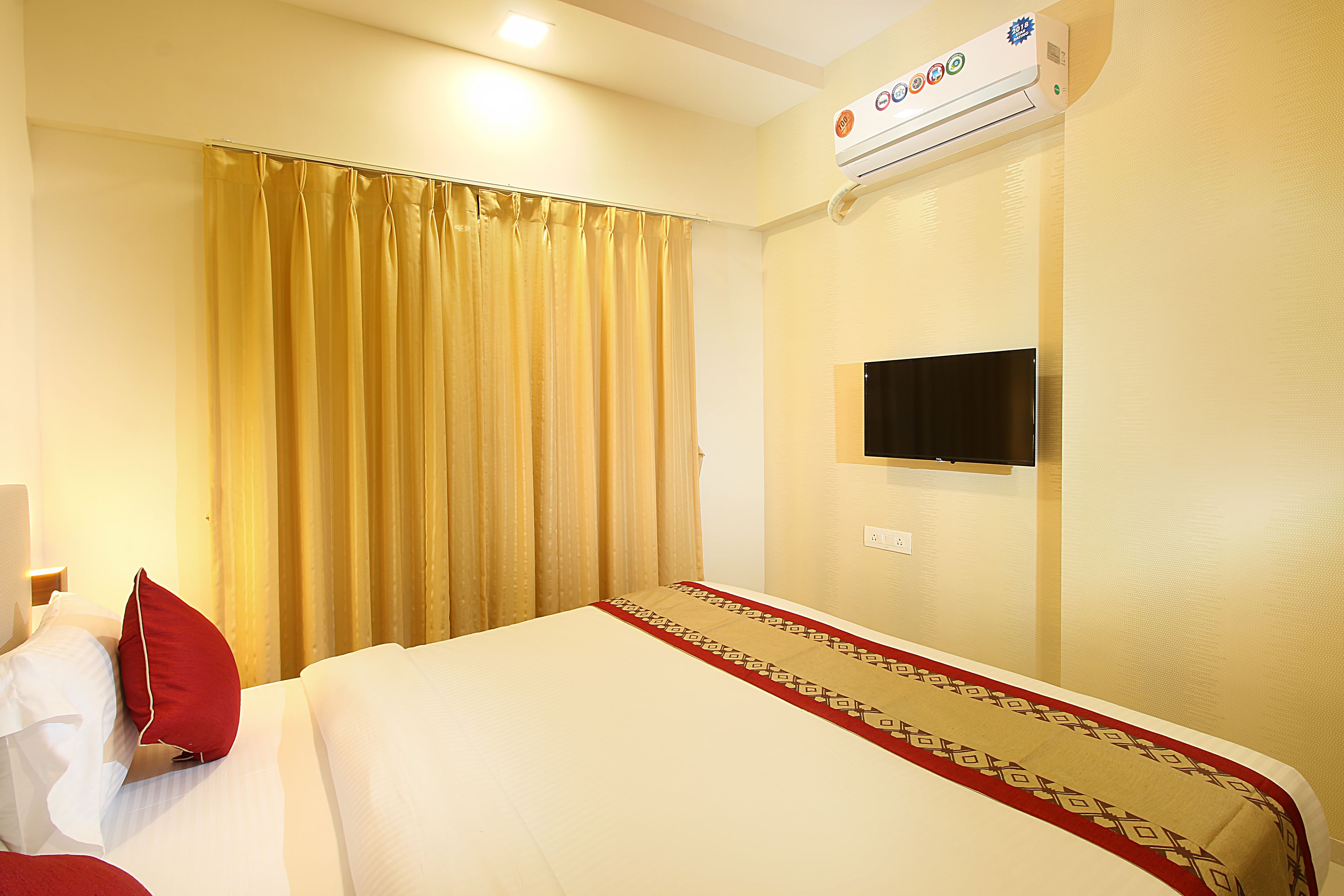 Una habitación de hotel con cama, cortinas, unidad de aire acondicionado y televisión.