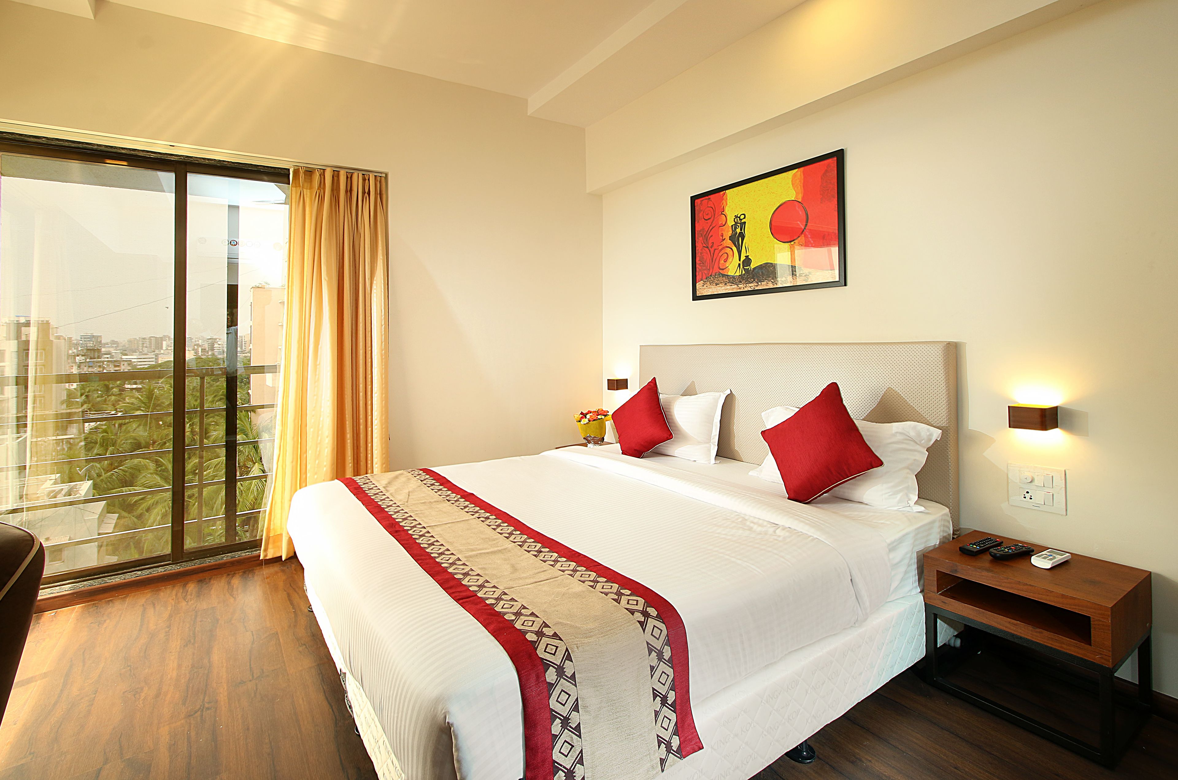 A hotel room with a large bed, a nightstand, a wall-mounted lamp, and a window with curtains.
