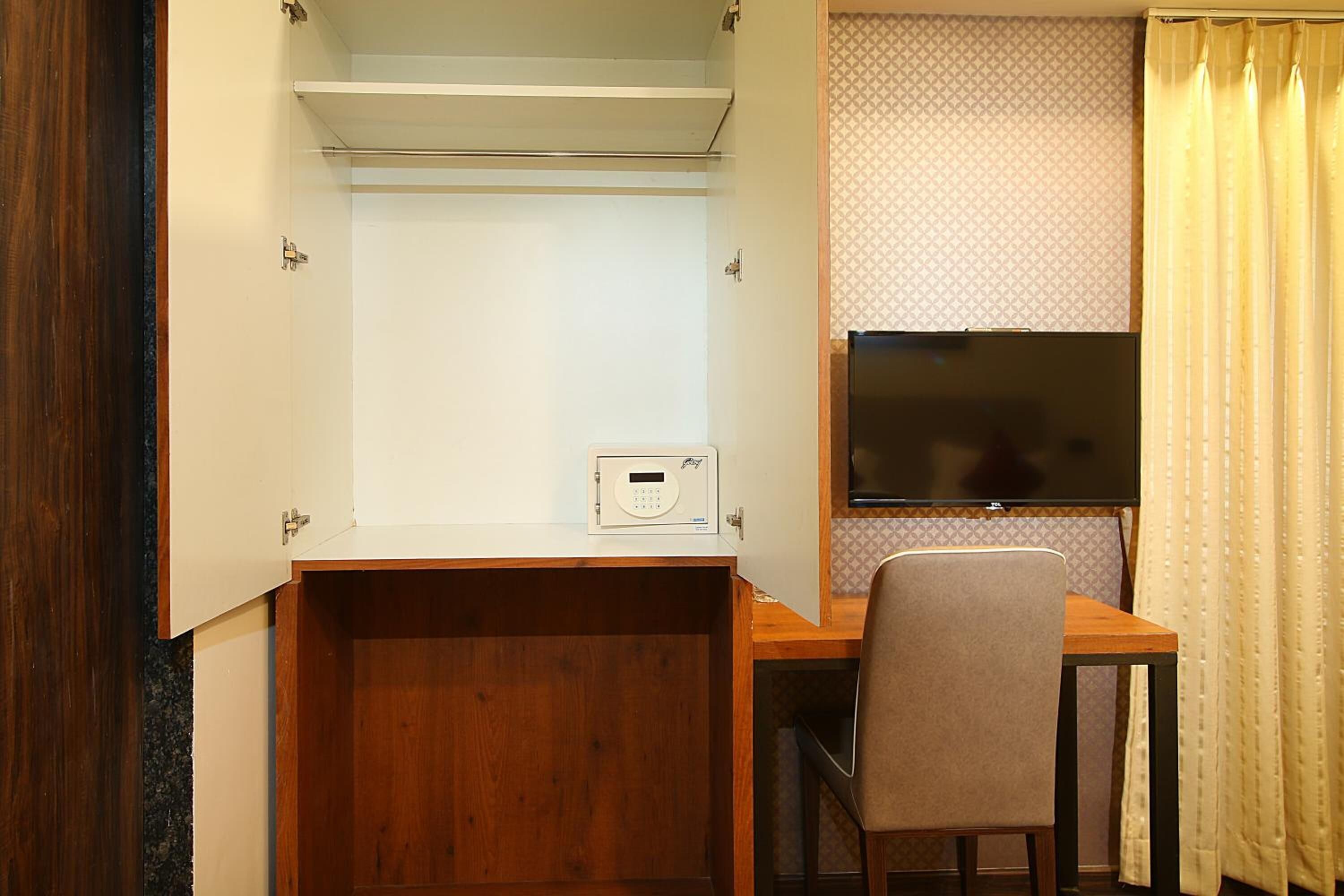 Habitación compacta con escritorio de madera, una silla, televisor y un pequeño dispositivo blanco sobre el escritorio.